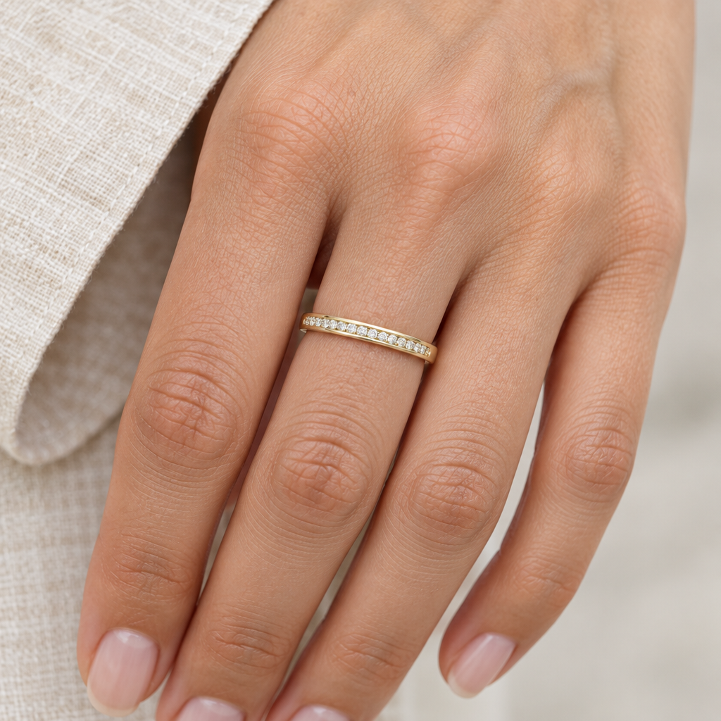 Slim 10K yellow gold diamond band worn on a hand beside cream linen