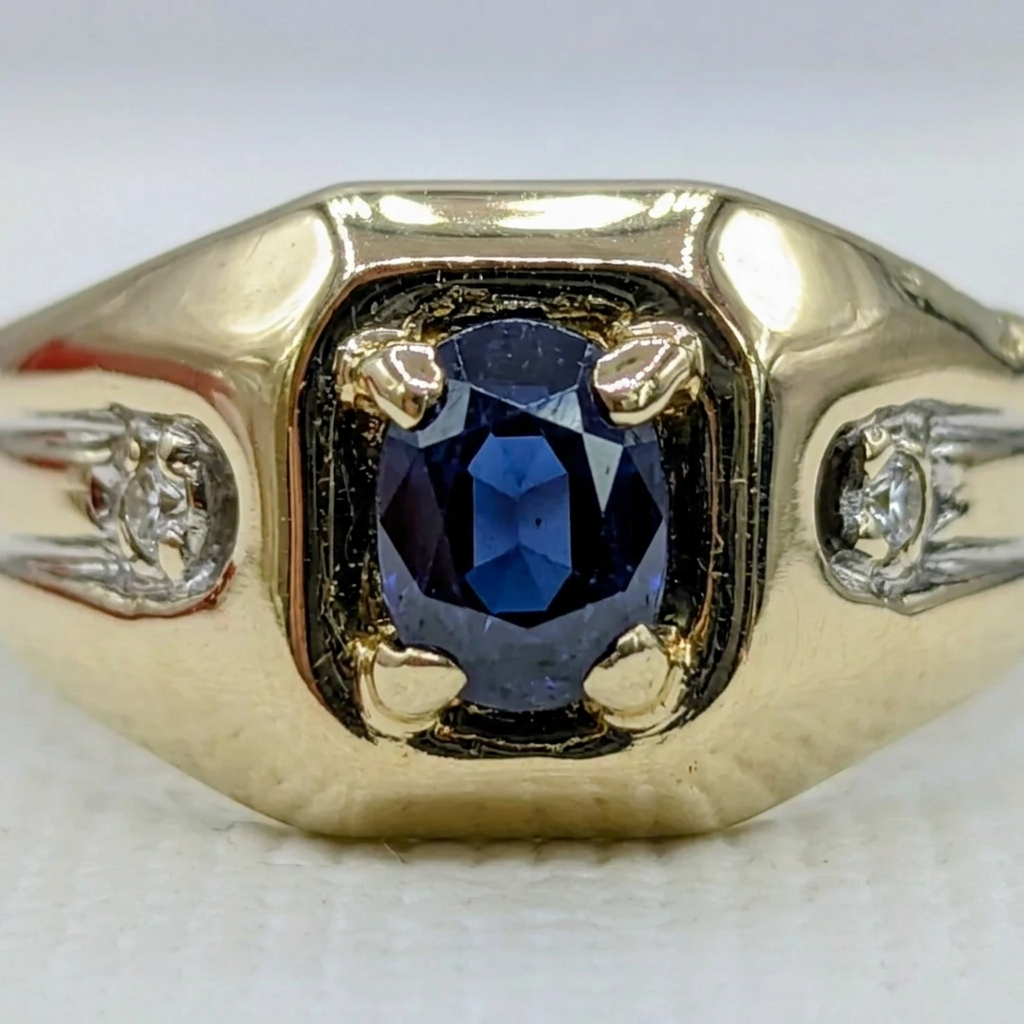 Macro close-up of the deep blue square sapphire in its polished yellow gold basket with corner prongs, flanked by diamond-set white gold shoulders