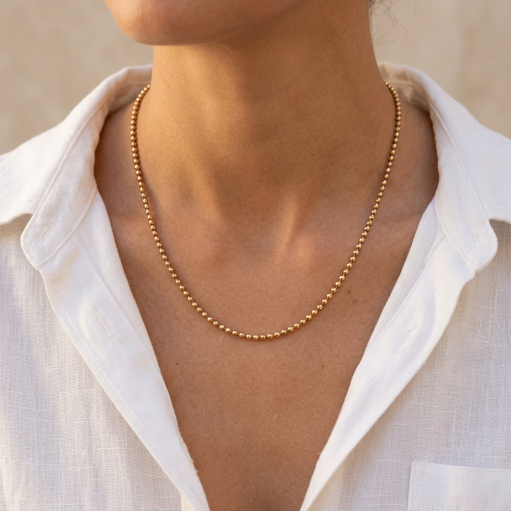 Model wearing a delicate 20-inch yellow gold ball chain with a white shirt