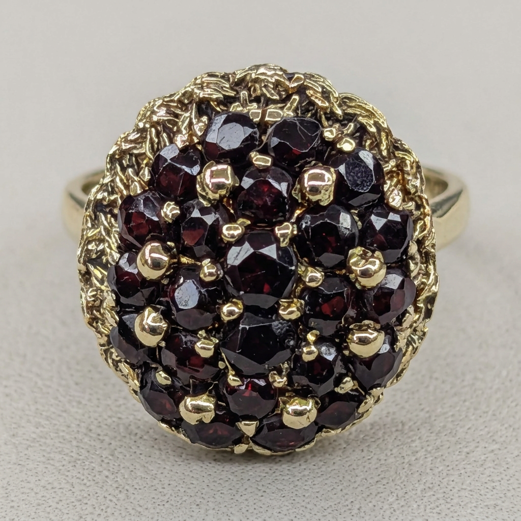 Close-up of dark red garnet cluster and ornate gold border on G100 ring
