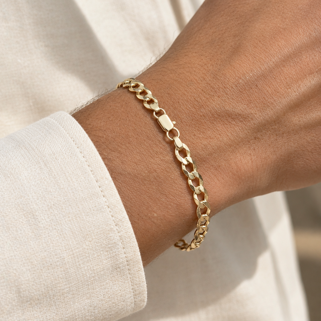 Yellow gold curb link bracelet worn on a wrist beside a cream cuff
